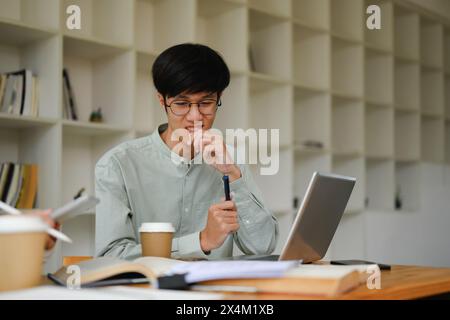 Asiatischer Student, der Laptop benutzt, um mit seinem Klassenkameraden in der Bibliothek im Internet zu recherchieren Stockfoto