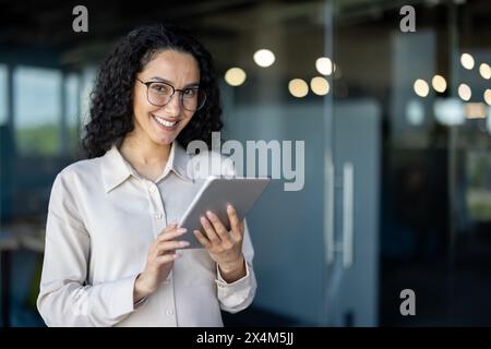 Junge und erfolgreiche Programmiererin, Porträt einer Ingenieurin mit Tablet-Computer-Startup-Arbeiterin, die in Bürogebäuden arbeitet und Tablets zum Testen von Anwendungen verwendet, lächelnd in die Kamera schaut. Stockfoto