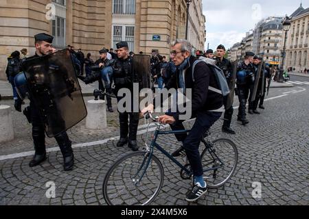 Ein Mann fährt mit dem Fahrrad an einer Linie der französischen Polizei vorbei, in der Nähe eines propalästinensischen Protests, der von Schülern vor dem Pantheon in Paris geführt wird. In einem Zeichen der Solidarität mit Palästina versammelten sich französische Gymnasiasten und Universitätsschüler vor dem Pantheon in Paris, verurteilten die anhaltende Gewalt in Gaza und forderten ein Ende dessen, was sie als Völkermord bezeichneten. Der friedliche pro-palästinensische Protest wurde mit der Anwesenheit der Polizei getroffen, die auch einen nahe gelegenen Pro-Israel-Gegenprotest leitete. Flaggen, Zeichen und Gesänge erfüllten die Luft, während beide Seiten ihre Sichtweise auf die Strömung zum Ausdruck brachten Stockfoto