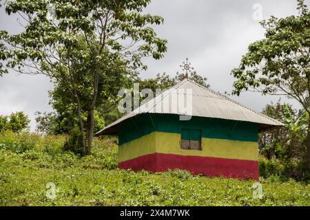 Eine bezaubernde orthodoxe Kirche in Äthiopien befindet sich auf einem ruhigen Hügel, lebhaft in den Farben der äthiopischen Flagge gemalt, mit auffälligen Kreuzen auf dem Dach Stockfoto