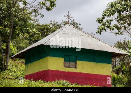 Eine bezaubernde orthodoxe Kirche in Äthiopien befindet sich auf einem ruhigen Hügel, lebhaft in den Farben der äthiopischen Flagge gemalt, mit auffälligen Kreuzen auf dem Dach Stockfoto