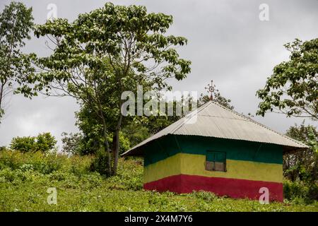 Eine bezaubernde orthodoxe Kirche in Äthiopien befindet sich auf einem ruhigen Hügel, lebhaft in den Farben der äthiopischen Flagge gemalt, mit auffälligen Kreuzen auf dem Dach Stockfoto