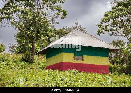 Eine bezaubernde orthodoxe Kirche in Äthiopien befindet sich auf einem ruhigen Hügel, lebhaft in den Farben der äthiopischen Flagge gemalt, mit auffälligen Kreuzen auf dem Dach Stockfoto