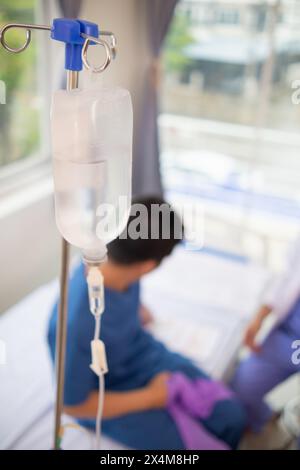 Ein Eisenständer zum Aufhängen der Kochsalzflasche zur Abgabe von Kochsalzlösung über einen Katheter an einen intravenösen Patienten, der auf dem Patientenbett liegt. Medizinisches Konzept in dem Docto Stockfoto