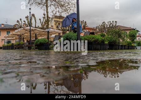 Hübsche Frau mittleren Alters, die im Regen mit einem Schirm auf einem kleinen Platz in Stresa Italien stand Stockfoto