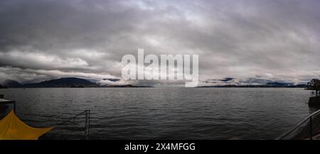 Panorama des Lago Maggiore an einem regnerischen Tag mit schweren niedrigen Wolken, die einen Teil der Küste bedecken - Reise- und Urlaubskonzept Stockfoto