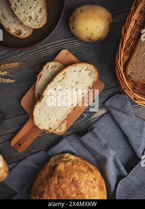 Rustikale Einrichtung mit frisch gebackenem Brot, Kartoffeln und Weizenohren auf dunklem Holzhintergrund Stockfoto