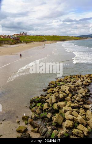 Eine Strandverteidigung mit Touristen in der Ferne, Whitby, North Yorkshire, Großbritannien, aus einem Haufen großer Felsbrocken. Stockfoto