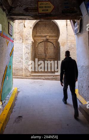 Ein junger Mann, der durch eine enge Gasse in den labyrinthartigen Straßen der Fez Medina in Marokko läuft. Stockfoto