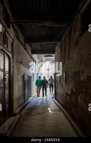 Junge Männer, die durch eine enge Gasse in den labyrinthartigen Straßen der Fez Medina in Marokko laufen. Stockfoto