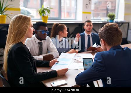 Multirassisches Geschäftsteam im Büro analysiert Daten in Diagrammen und Diagrammen. Weiße Frau, afrikanischer Mann und Kollegen planen Strategien. Unternehmensgruppe Stockfoto