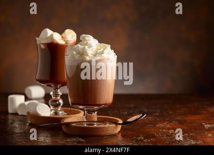 Heiße Schokolade mit Schlagsahne in einem Glasbecher auf einem alten braunen Tisch. Kopierbereich. Stockfoto