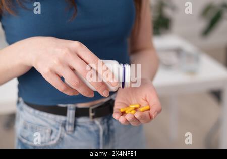 Junge Frau hält gelbe Pillen in der Hand, Frau nimmt Nahrungsergänzungsmittel und Vitamine aus einer Flasche, Nahaufnahme Stockfoto