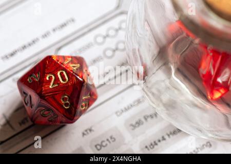 Rote D20 Würfel neben einem Glasglas auf einem Zeichenblatt, wobei der Schwerpunkt auf Strategie und Entscheidungsfindung in Rollenspielen liegt. Stockfoto