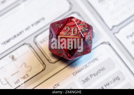 Fokussierter Schuss eines roten D20-Würfel auf einem Zeichenblatt, der kritische Spielmomente in Tabletop-Rollenspielen hervorhebt. Stockfoto