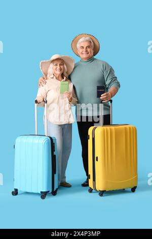 Reifes Paar mit Pässen und Koffern bereit für den Sommerurlaub auf blauem Hintergrund Stockfoto