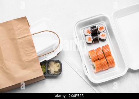 Plastikbehälter mit leckeren Sushi-Rollen, Essstäbchen und Papiertüte auf weißem Grunge-Hintergrund. Lieferkonzept Stockfoto