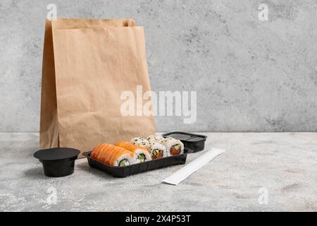 Plastikteller mit leckeren Sushi-Rollen, Essstäbchen und Papiertüte auf hellem Grunge-Hintergrund. Lieferkonzept Stockfoto