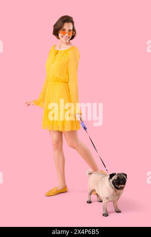 Junge Frau mit niedlichem Mops-Hund an der Leine vor rosa Hintergrund Stockfoto