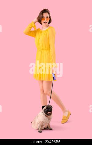 Junge Frau mit niedlichem Mops-Hund an der Leine vor rosa Hintergrund Stockfoto