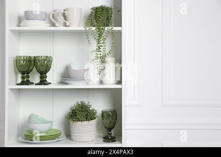 Verschiedene saubere Geschirr und Zimmerpflanzen auf den Regalen im Schrank drinnen Stockfoto