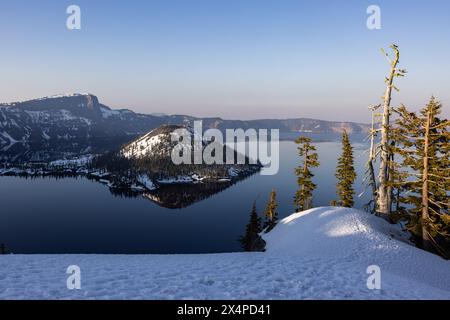 Ein schneebedeckter Nachmittag im Crater Lake National Park. Der See ist ruhig und spiegelt Zauberer Island wider. Stockfoto