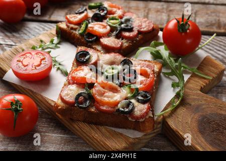 Leckere Pizzastoasts, Tomaten und Rucola auf Holztisch, Nahaufnahme Stockfoto