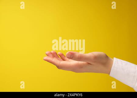 Frau, die etwas in der Hand hält auf gelbem Hintergrund, Nahaufnahme. Leerzeichen für Text Stockfoto