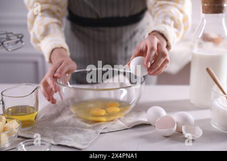 Teig herstellen. Frau bricht Ei am weißen Tisch in der Küche, Nahaufnahme Stockfoto