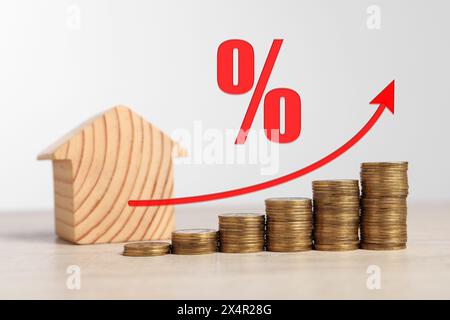 Hypothekenzinssatz. Hölzernes Modell des Hauses, gestapelte Münzen, Pfeil und Prozentzeichen Stockfoto