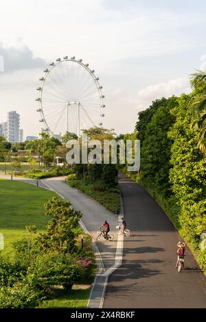 Singapur - August 29,2023 : Eine Familie kann das Radfahren in den Gardens by the Bay mit dem Hintergrund Singapore Flyer sehen. Stockfoto