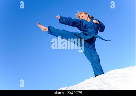 Junge Frau in blauem Kimono steht auf Schnee und trainiert tritt Stockfoto