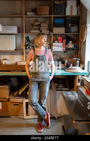 Entspannte Tischlerin, die Zeit am Arbeitsplatz verbringt, macht Pause in der Tischlerei mit Blick auf das Fenster. Stockfoto