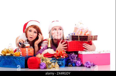 Zwei hübsche Frauen in weihnachtlicher Kleidung liegen auf weißem Boden mit Geschenken, isoliert auf weiß Stockfoto