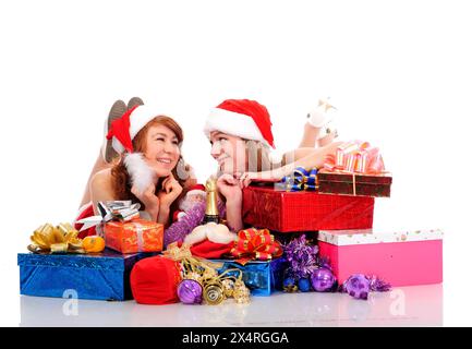 Zwei hübsche Frauen in weihnachtlicher Kleidung liegen auf weißem Boden mit Geschenken, isoliert auf weiß Stockfoto