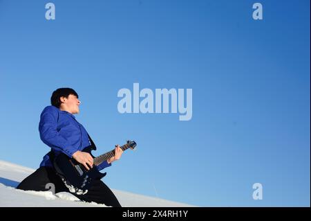 Musiker, der auf der Elektrogitarre in der Schneelage spielt Stockfoto