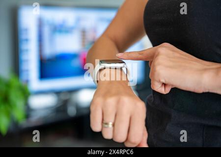 Junge Frau, die auf Fitness-Tracker blickt und Herzfrequenz, Schrittzählung und verbrannte Kalorien anzeigt. Smart Watch auf weiblicher Hand, Standpunkt, Konzept von Stockfoto