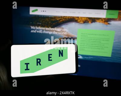 Person, die ein Mobiltelefon mit dem Logo des australischen Bitcoin-Bergbauunternehmens Iris Energy Ltd. (IREN) vor der Webseite hält. Schwerpunkt auf dem Display des Telefons. Stockfoto