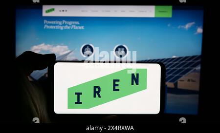 Person, die ein Mobiltelefon mit dem Logo des australischen Bitcoin-Bergbauunternehmens Iris Energy Ltd. (IREN) vor der Webseite hält. Schwerpunkt auf dem Display des Telefons. Stockfoto