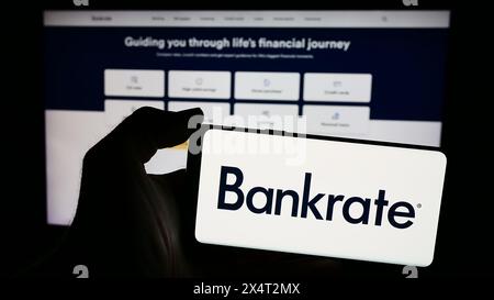 Person mit Smartphone und Logo des US-amerikanischen Finanzunternehmens Bankrate LLC vor der Website. Schwerpunkt auf dem Display des Telefons. Stockfoto