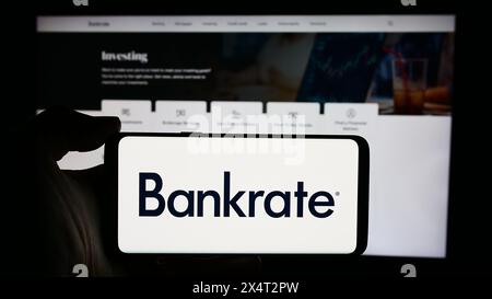 Person, die ein Mobiltelefon mit dem Logo des US-amerikanischen Finanzunternehmens Bankrate LLC vor der Website des Unternehmens hält. Schwerpunkt auf dem Display des Telefons. Stockfoto