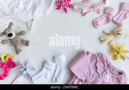 Set mit pinkfarbenen Kleidern und Accessoires für Neugeborene. Gestricktes Spielzeug Hase und Hund, Strampler, Socken und Handband auf weißem Holzhintergrund. Babydusche Stockfoto