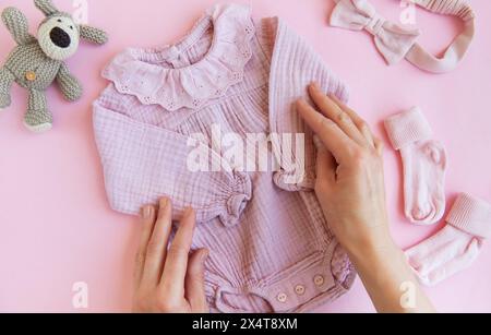 Rosafarbener Body mit Spielzeug gestricktem Hund, Socken und Stirnband. Set Babykleidung und Accessoires Sommer auf rosa Hintergrund. Fashion Neugeborene. Flach, oben Stockfoto