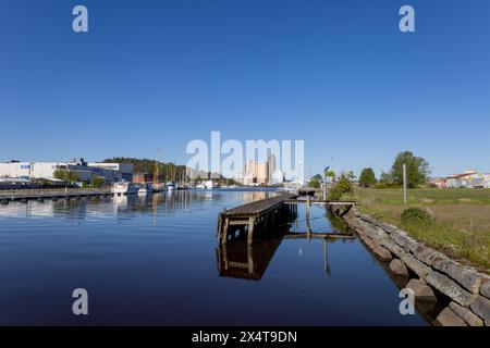 Uddevalla, Schweden - 29. Mai 2021: Kanaleingang und Steinkai mit Holzbrücke. Boote, die entlang des Kanals vertäut sind. Industriegebäude im Hintergrund. Keine Anzeige Stockfoto