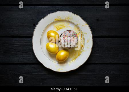 Hausgemachter Osterkuchen und goldfarbene Eier stehen auf einem Teller auf einer schwarzen Tafel, Osterferien in der Ukraine Stockfoto