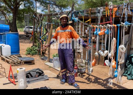 afrikanischer Straßenhändler, der neben der Straße Hardware verkauft, trägt orangefarbene Arbeitskleidung und Dreadlocks-Zöpfe Stockfoto