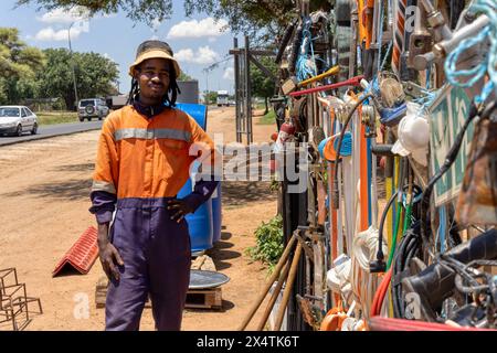 afrikanischer Straßenhändler, der neben der Straße Hardware verkauft, trägt orangefarbene Arbeitskleidung und Dreadlocks-Zöpfe Stockfoto