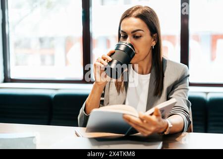 Frau, die in einem Büro arbeitet und Kaffee aus einer Thermoskanne trinkt Stockfoto