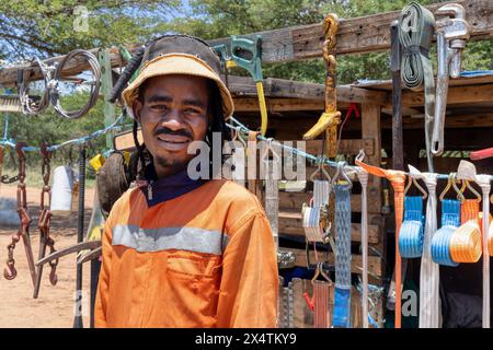 afrikanischer Straßenhändler, der neben der Straße Hardware verkauft, trägt orangefarbene Arbeitskleidung und Dreadlocks-Zöpfe Stockfoto