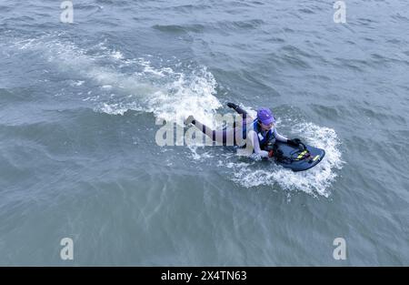 (240505) -- FUZHOU, 5. Mai 2024 (Xinhua) -- Ein Drohnenfoto zeigt eine junge Frau, die Motorsurfen im Minjiang-Fluss in der Stadt Jingxi in der südöstlichen chinesischen Provinz Fujian erlebt, 27. April 2024. Das Oasis Camp in Jingxi Stadt Fuzhou liegt im Minjiang-Flussbecken und ist umgeben von üppigen grünen Bergen und klarem Wasser, was es zu einem beliebten Reiseziel für Outdoor-Wassersport macht. In den letzten Jahren haben sich Motorsurfen, Kajakfahren und Paddleboarding zu den „neuen Favoriten“ für die jungen Menschen hier entwickelt. Auf dem Paddelbrett liegend, auf den blauen Himmel blickend, weiße Wolken, Stockfoto